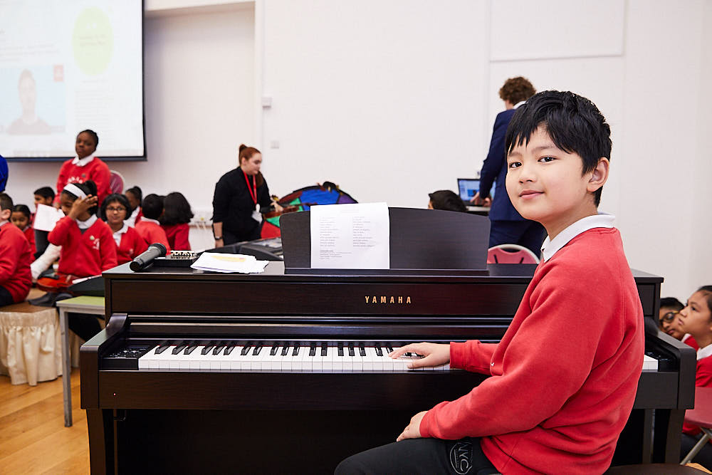 Primary school pupil is sat at a Yamaha digital piano. 