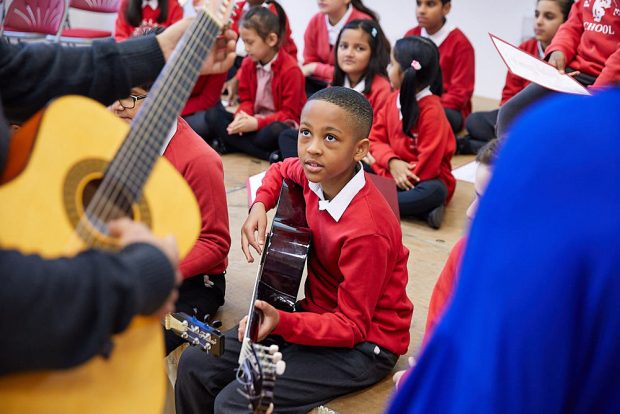 Group of primary school children sitting on the floor playing guitars.