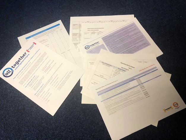 Several documents on the floor, detailing the all together programme guidance.