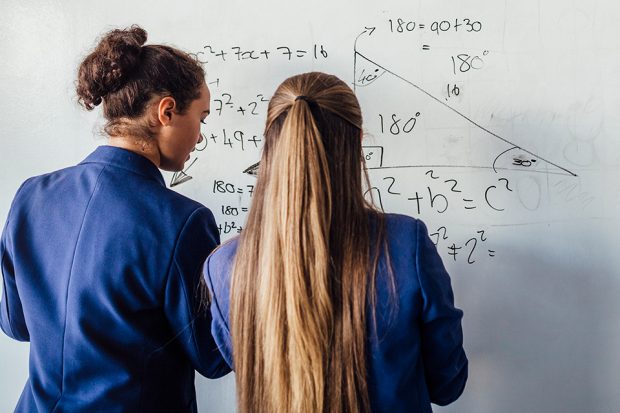 Two female pupils solving maths problem on whiteboard