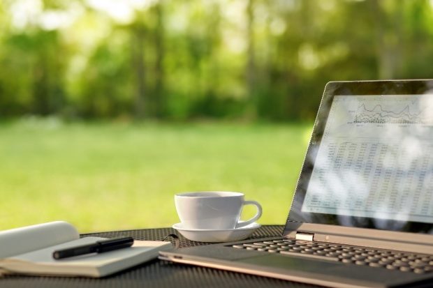 A laptop and a mug of tea sit on a table in a garden