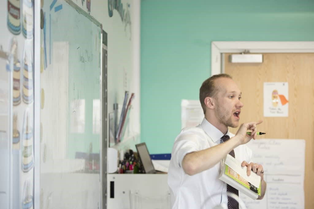 Jon Hutchinson gesturing while speaking in front of a whiteboard