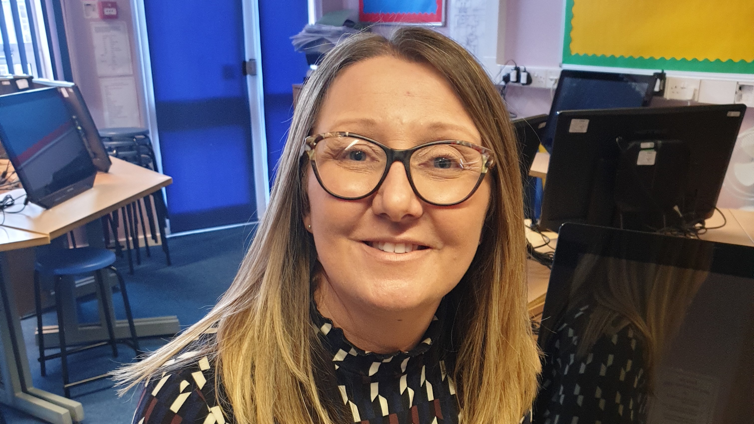 A young woman wearing glasses smiles at the camera