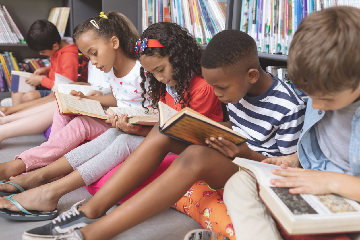 School children sitting on cushions and studying over books in a library 