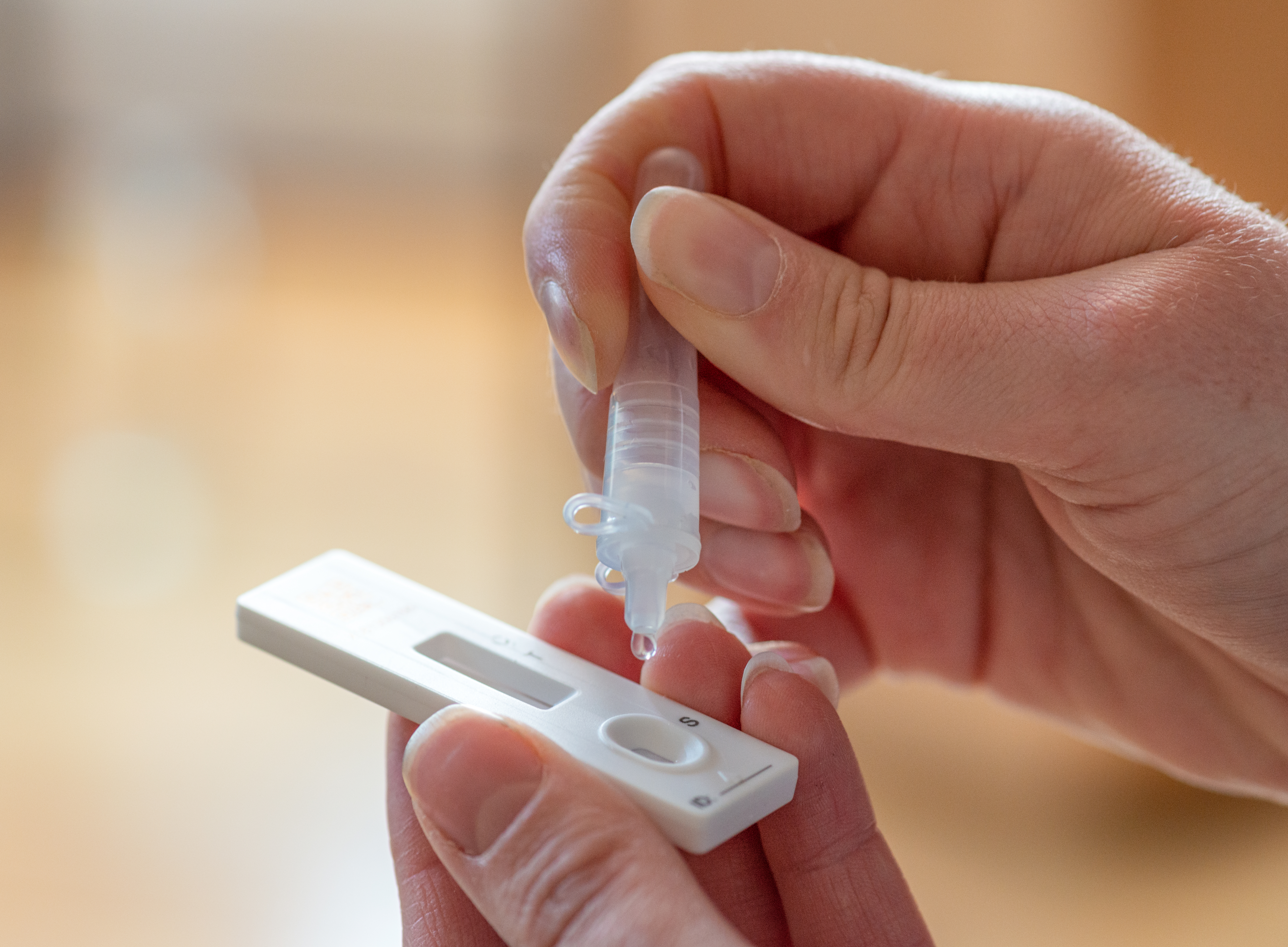 Close-up as a woman drips buffer solution from a plastic vial onto the lateral flow test device for Covid-19.