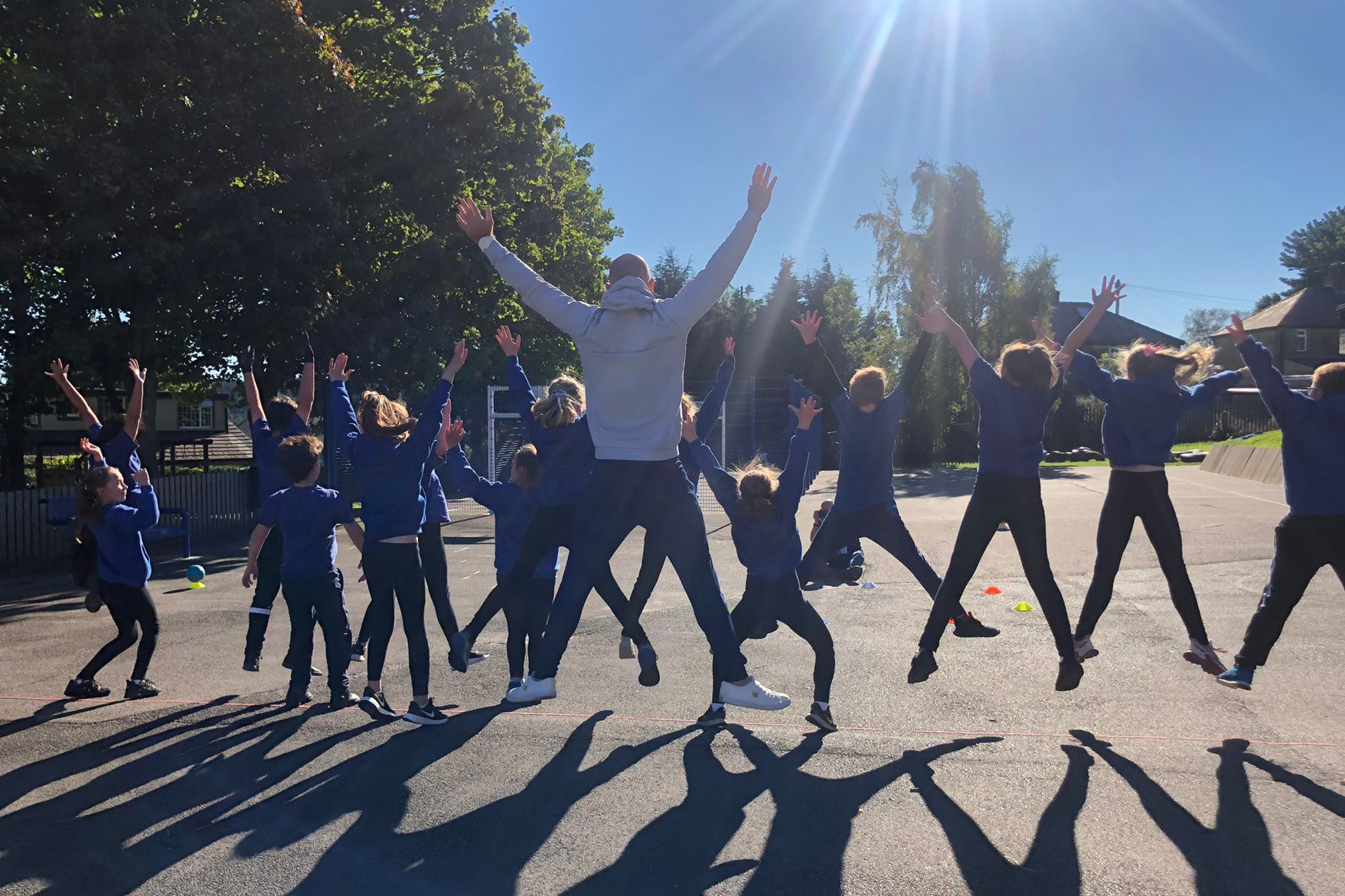 Children doing star jumps in the playground with their teacher during PE.