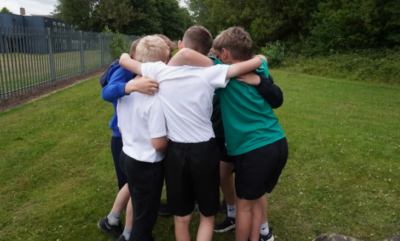 A group of pupils stood in a circle with their arms around each other.