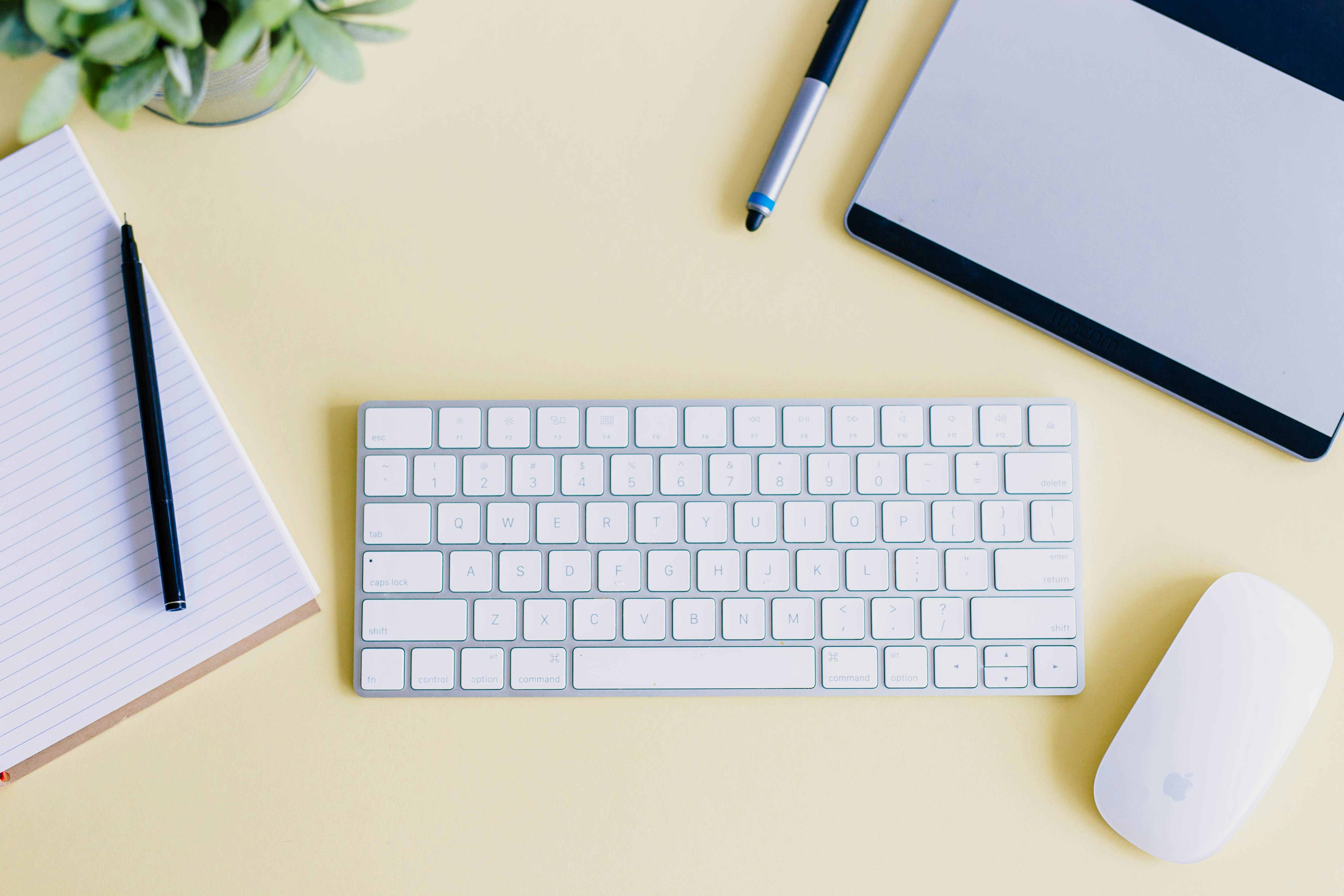 Laptop, keyboard, notepad and pen, and mouse on yellow surface